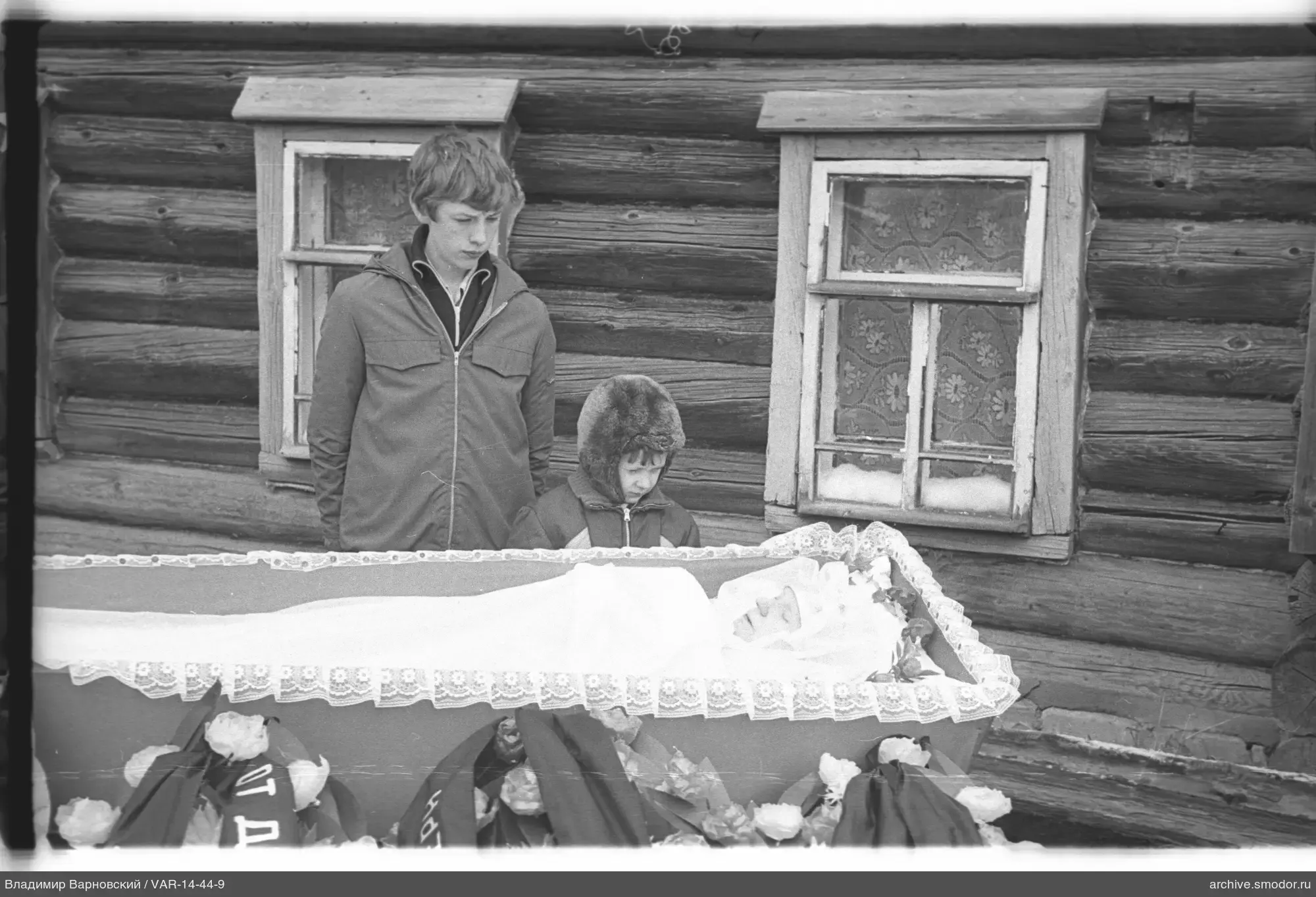 Two boys by a wooden house with coffin