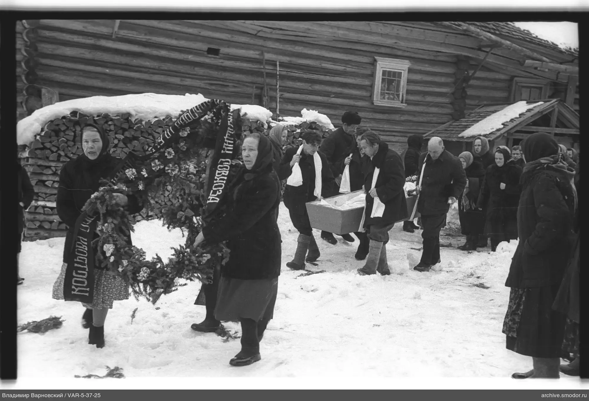 Gruppe von Menschen mit Sarg bei Holzhaus