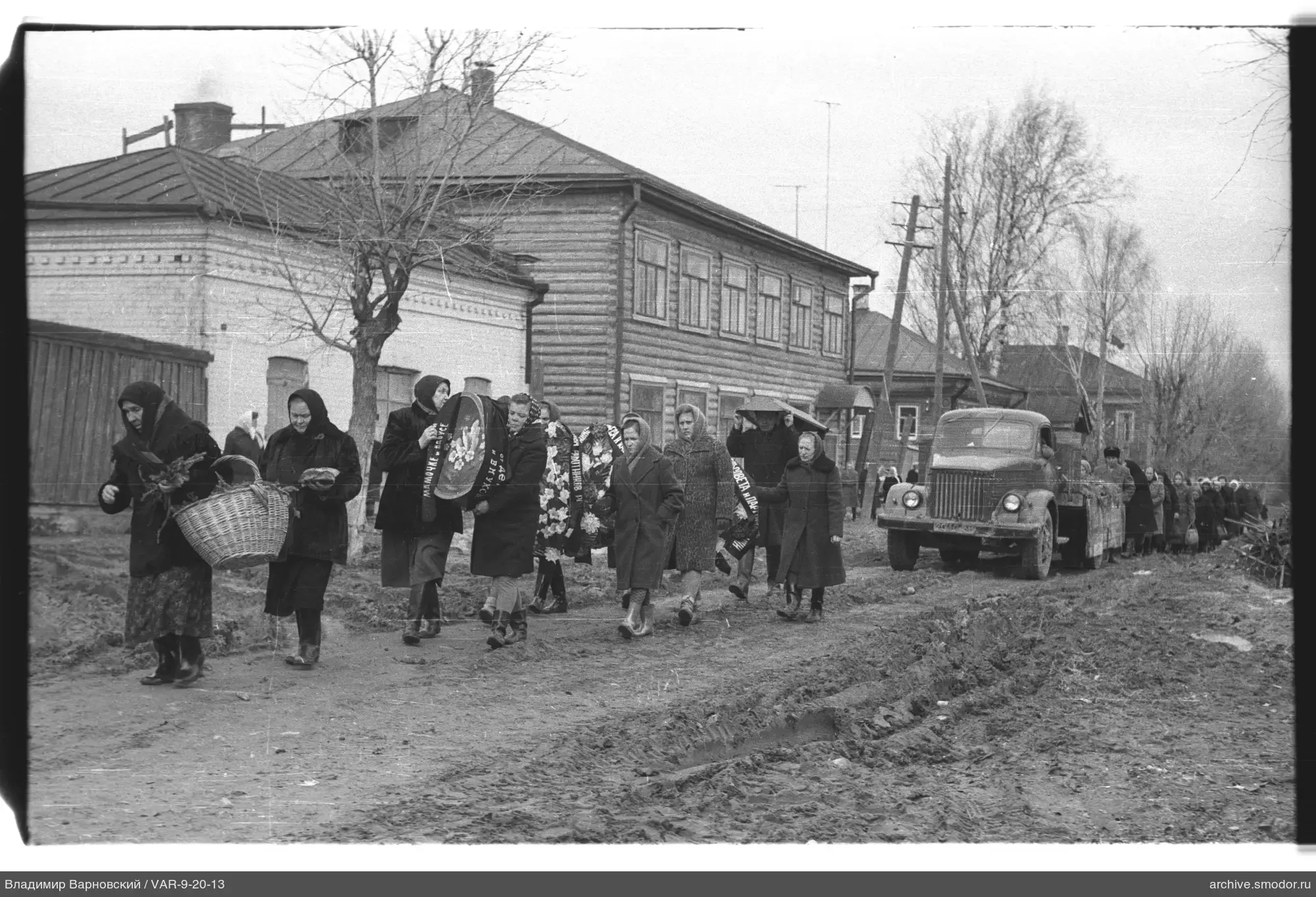 Gruppe von Menschen auf Straße mit Kränzen und Lastwagen