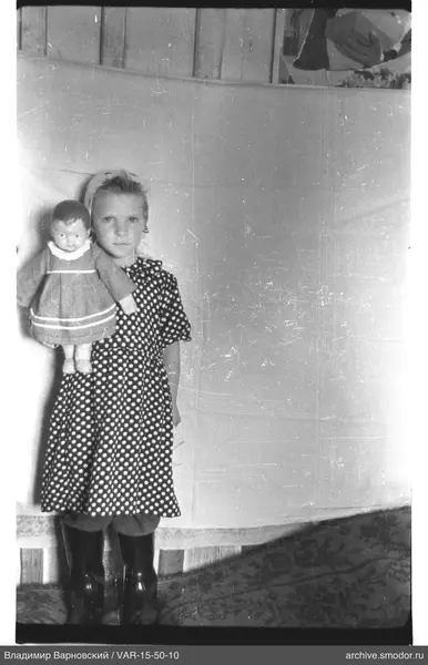 Mädchen mit Puppe in gepunktetem Kleid und Kopftuch