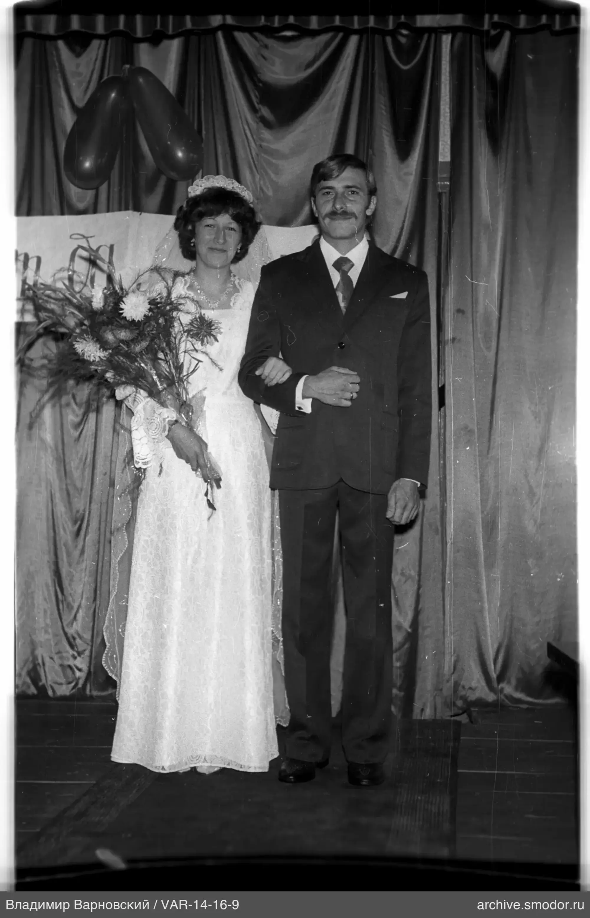 Couple with bouquet and balloons against curtains