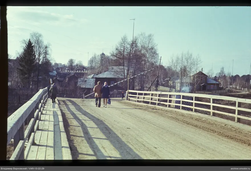 Holzbrücke mit Fußgängern und Häusern im Hintergrund