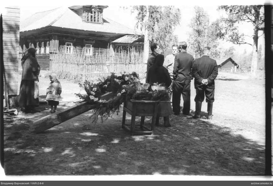 Мужчины и женщины у деревянного дома с носилками