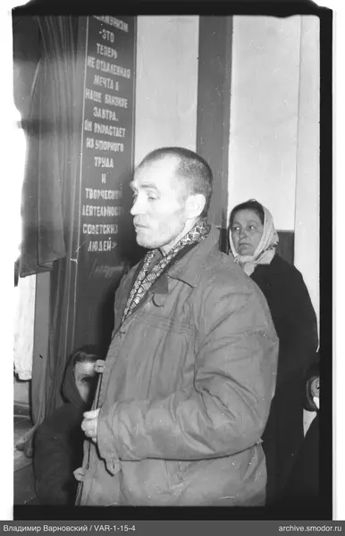 Мужчина с предметом и женщины на фоне плаката