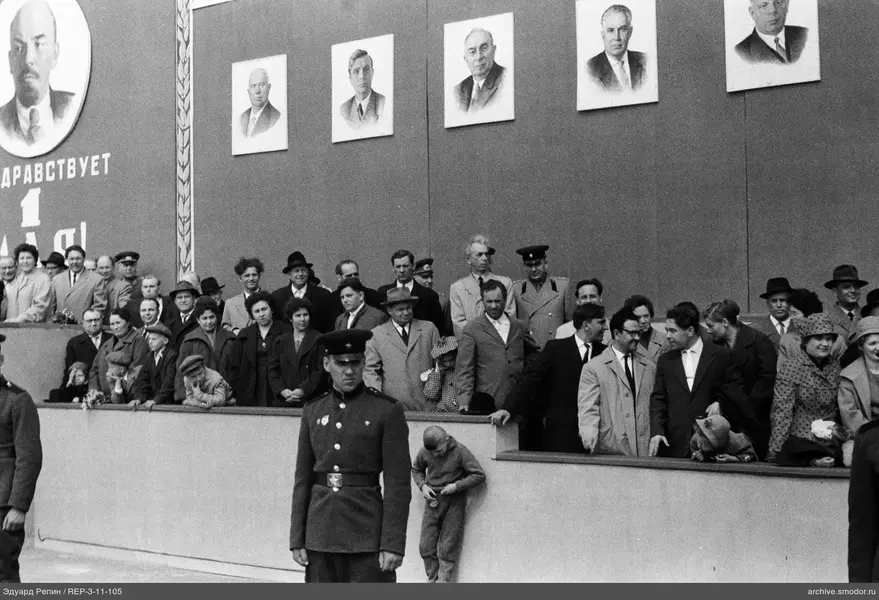 Группа на трибуне перед портретами и надписью