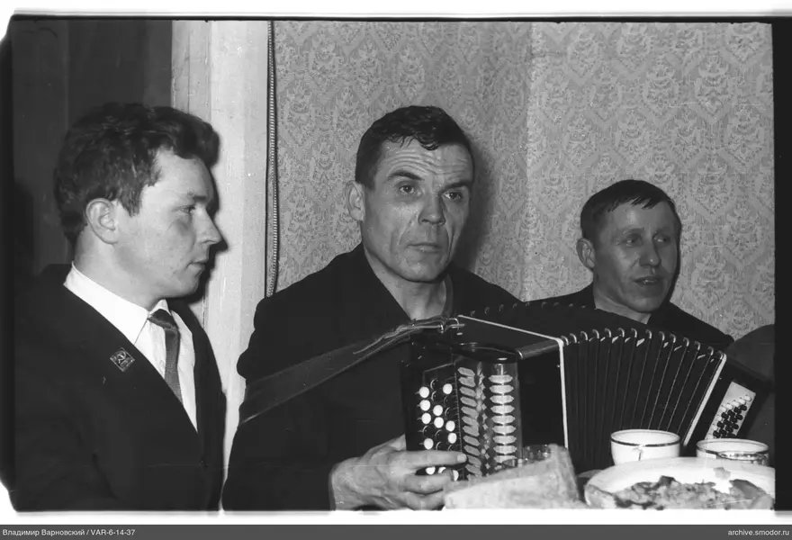 Three men at a table with a bayan and food