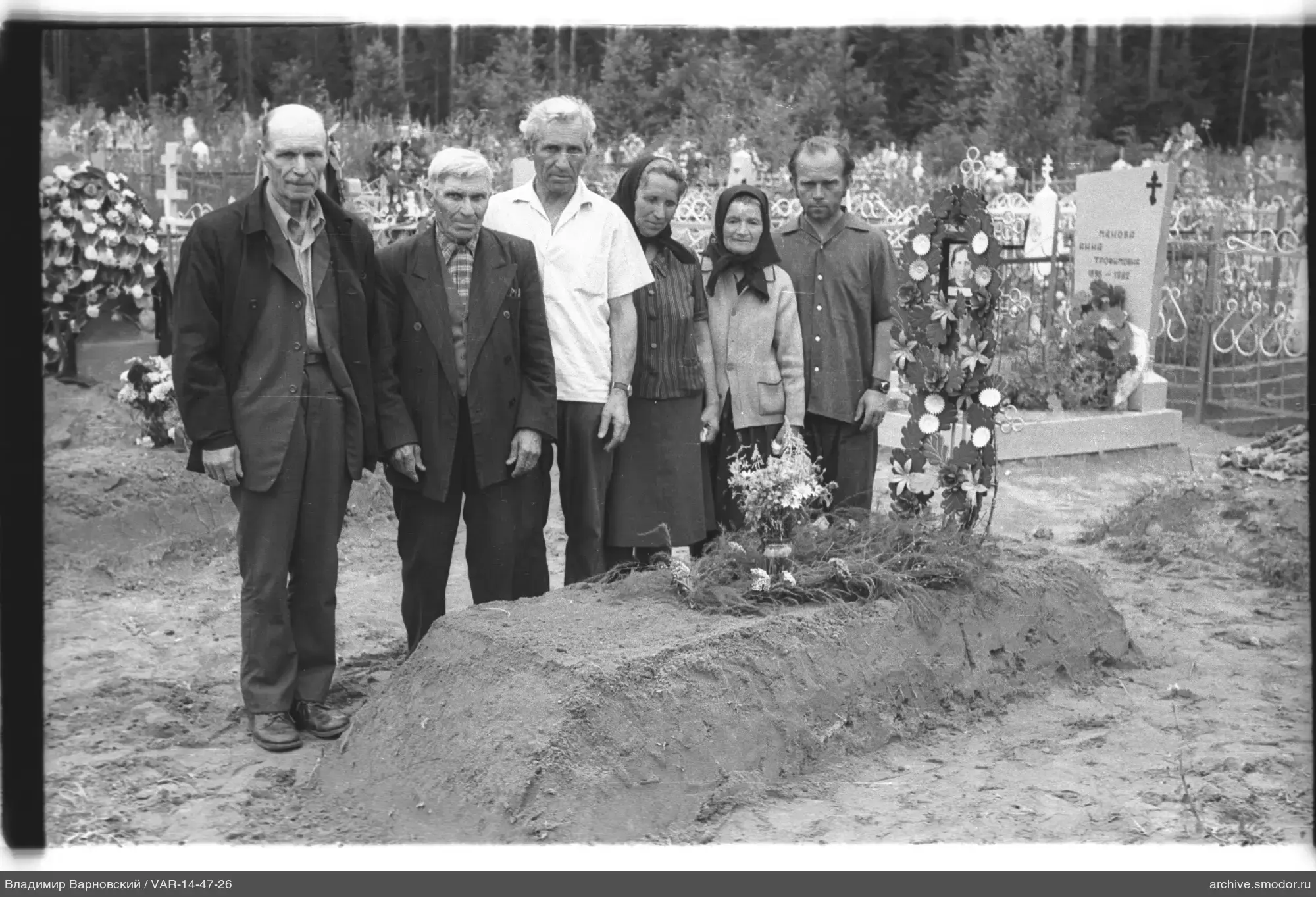 Gruppe vor frischem Grab mit Blumen