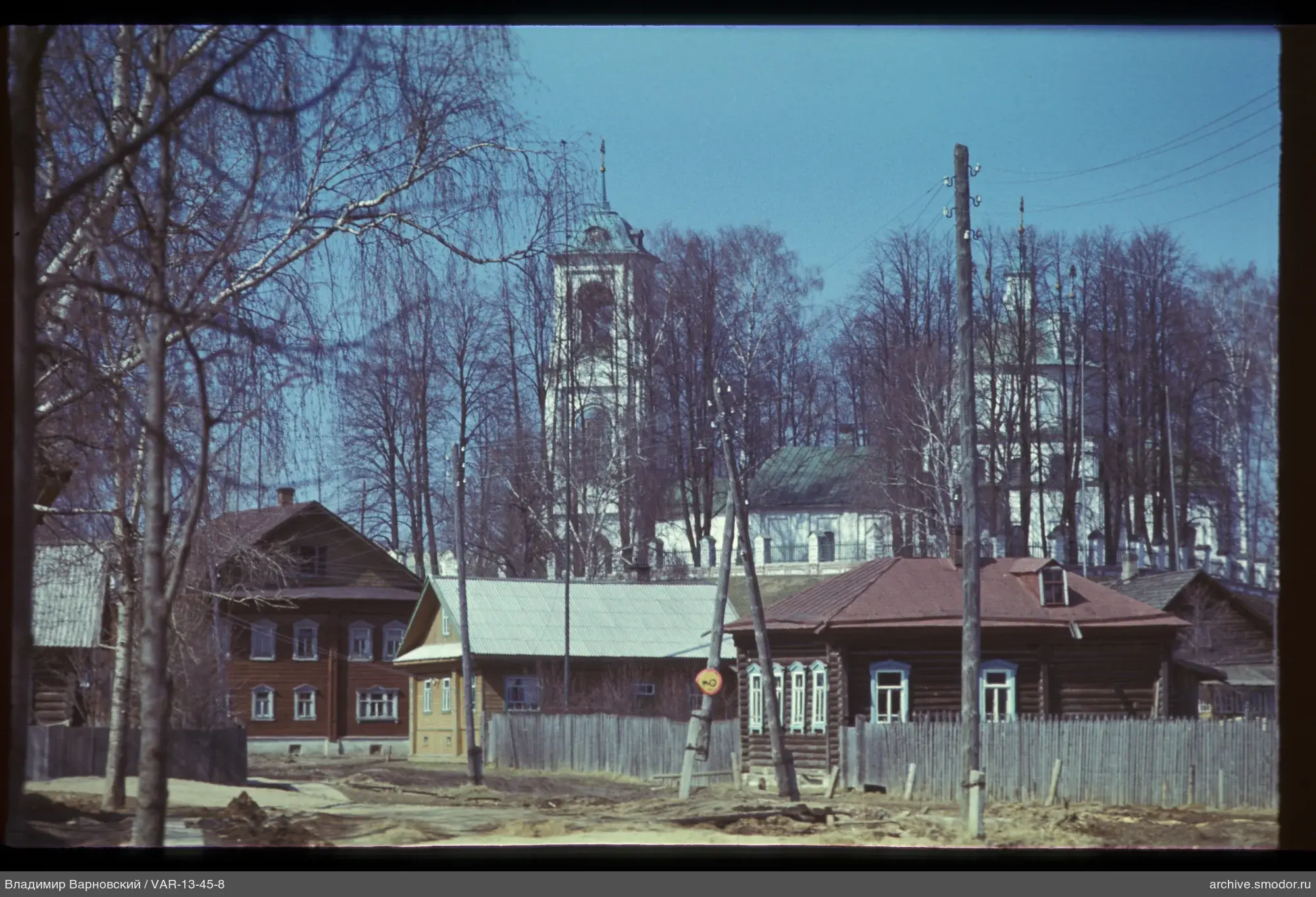 Holzhäuser und Kirche vor kahlblättrigen Bäumen