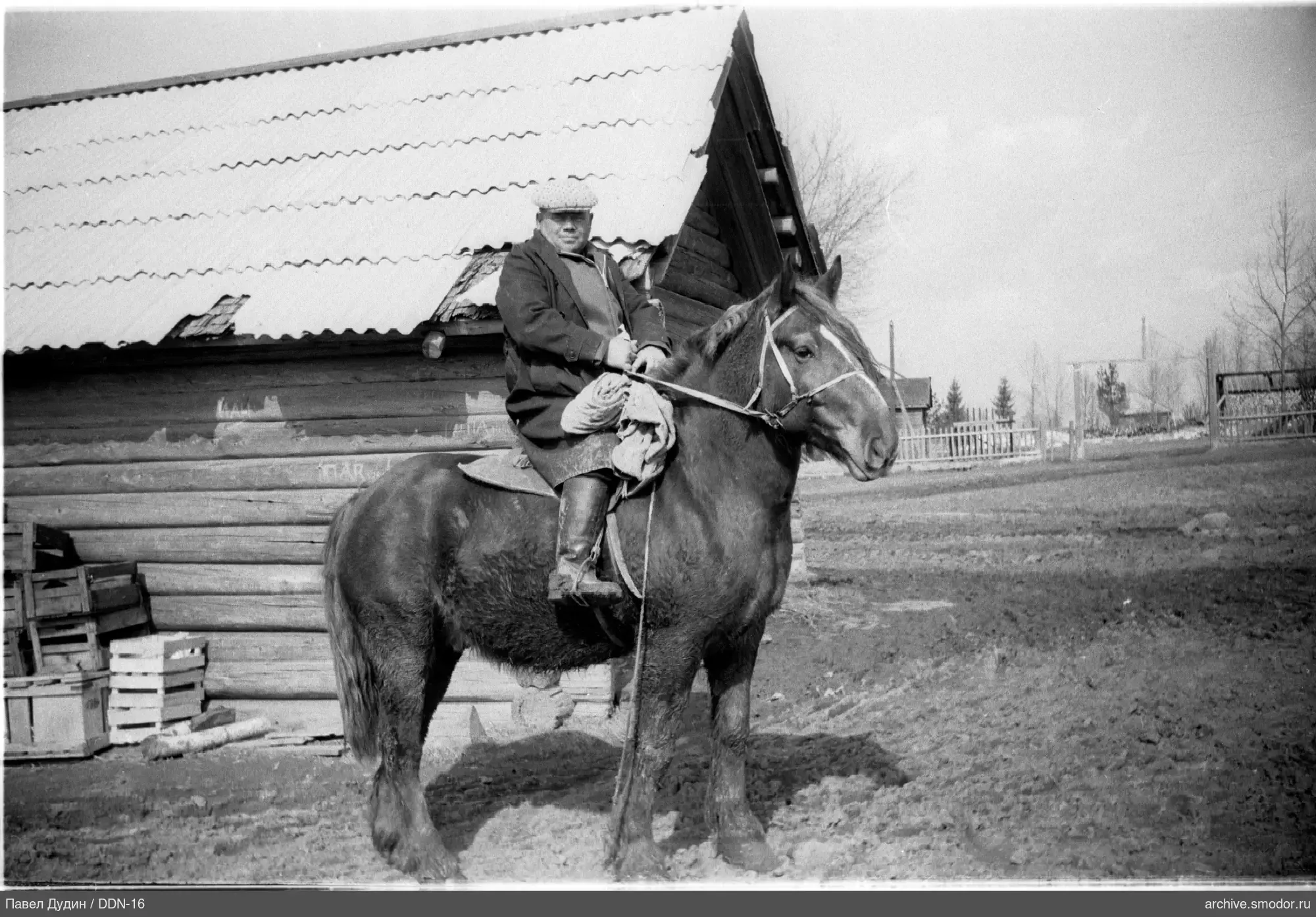 Mann auf einem Pferd vor einem Holzhaus