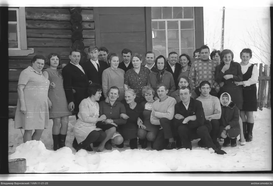 Gruppe von Menschen vor einem Holzhaus im Schnee