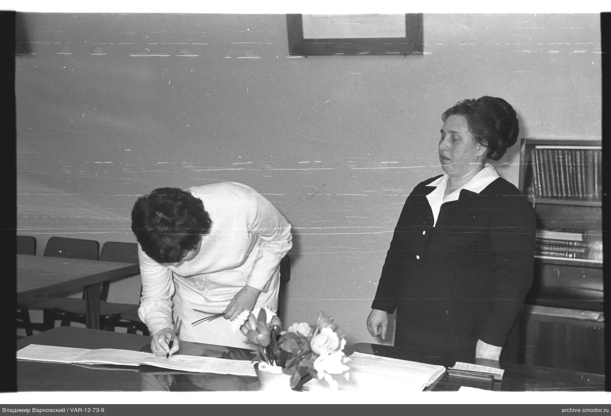 Two women at a table with a book and flowers