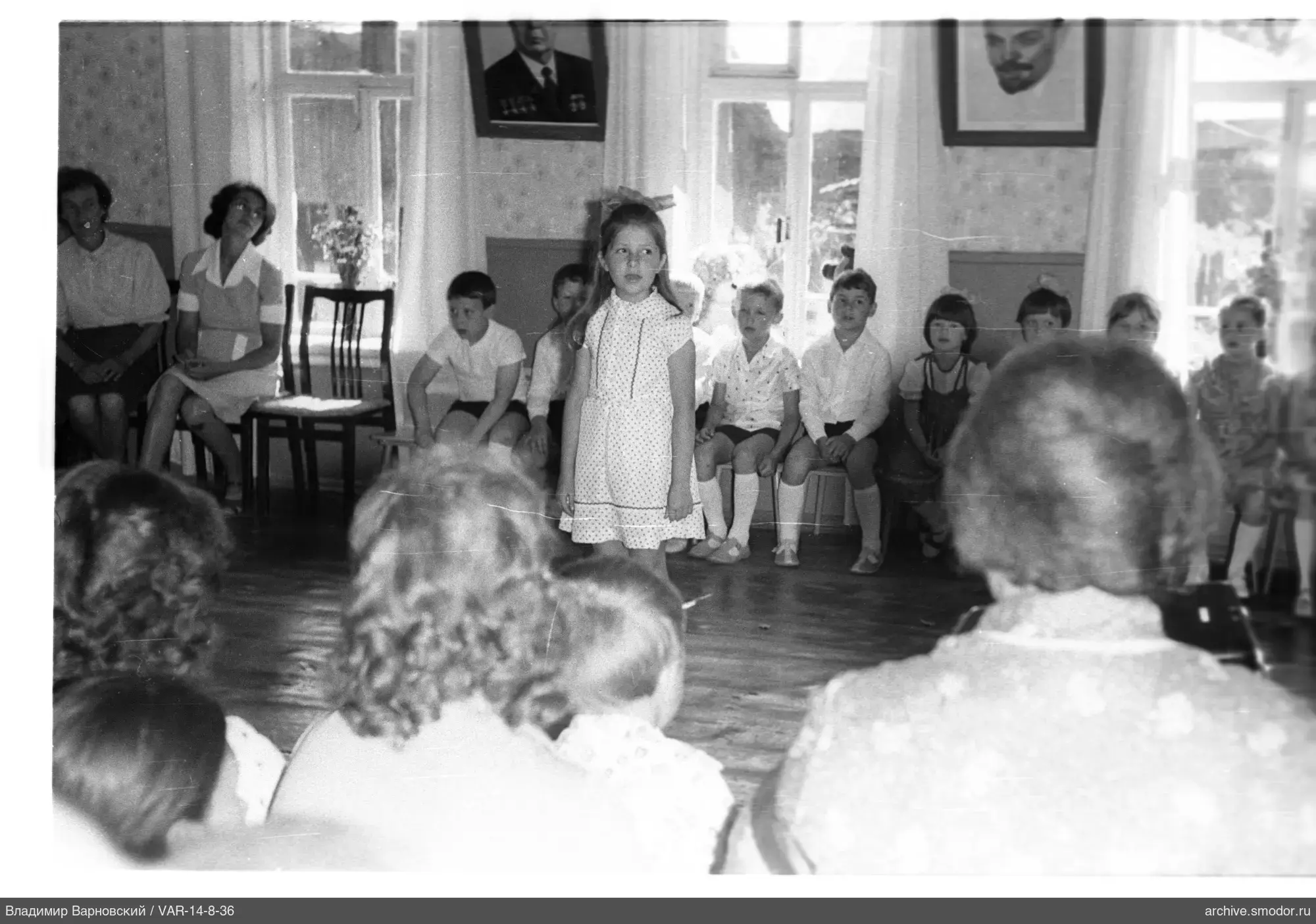 Girl in the center of the room with children and portraits