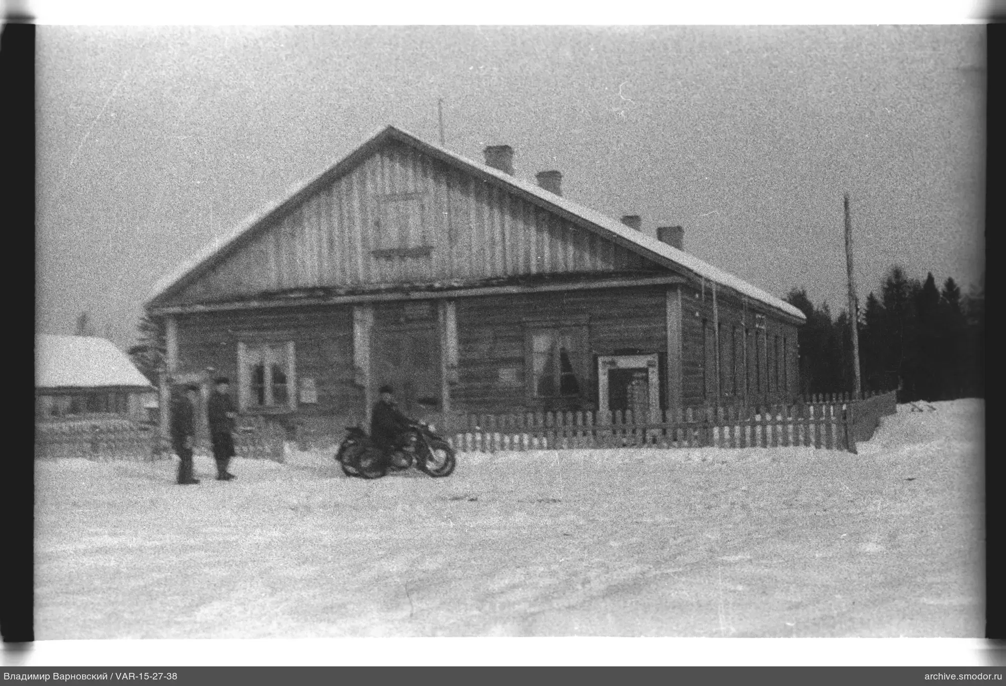 Holzgebäude mit Männern und Motorrad im Schnee