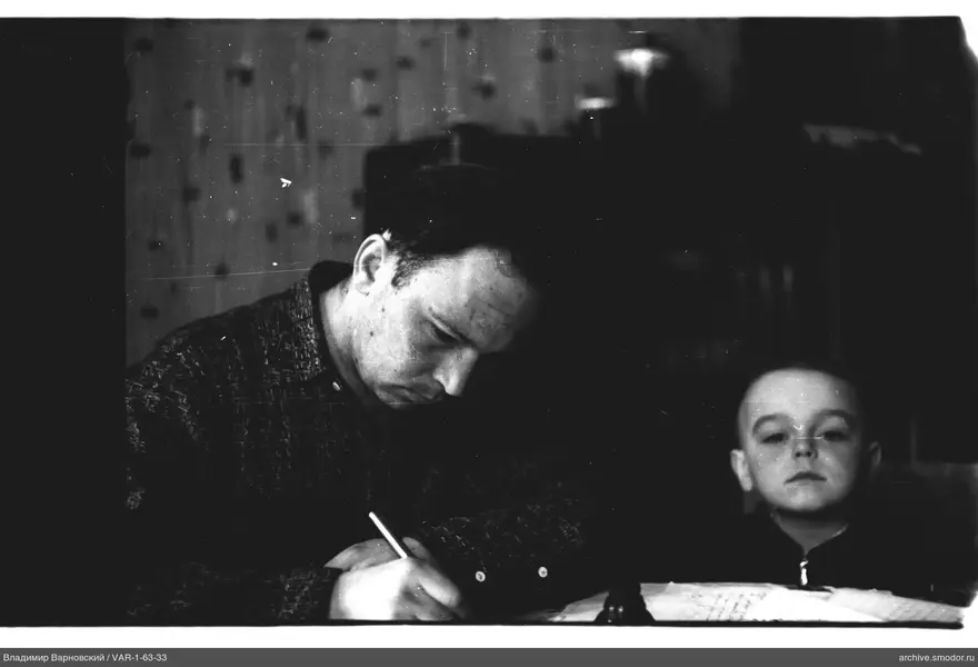 Man writing at a table with a boy nearby