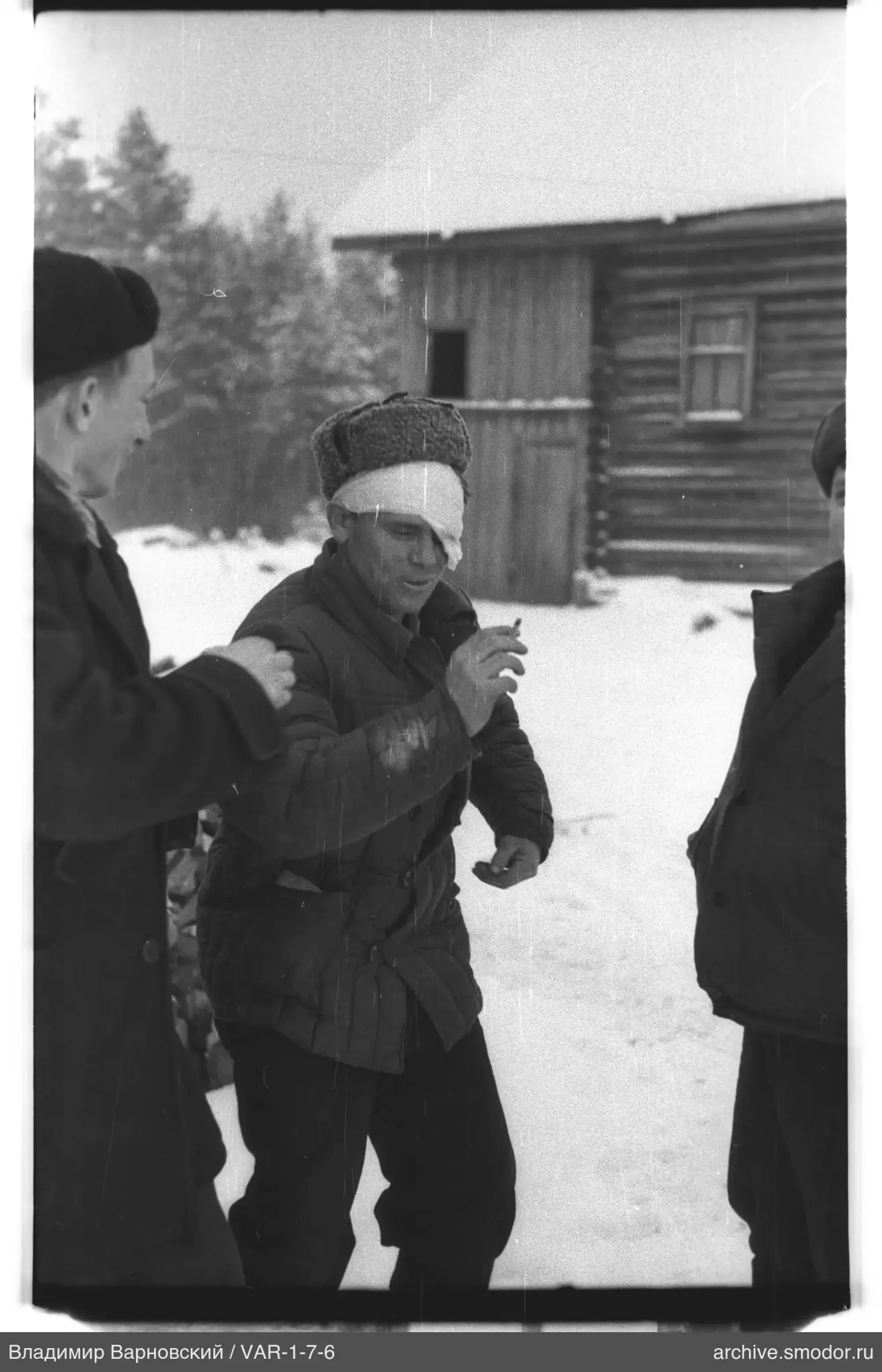 Drei Männer im Schnee neben einem Holzhaus