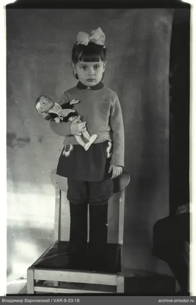 Mädchen mit Puppe auf Stuhl