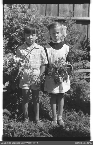Kinder mit Blumen vor Holzwand