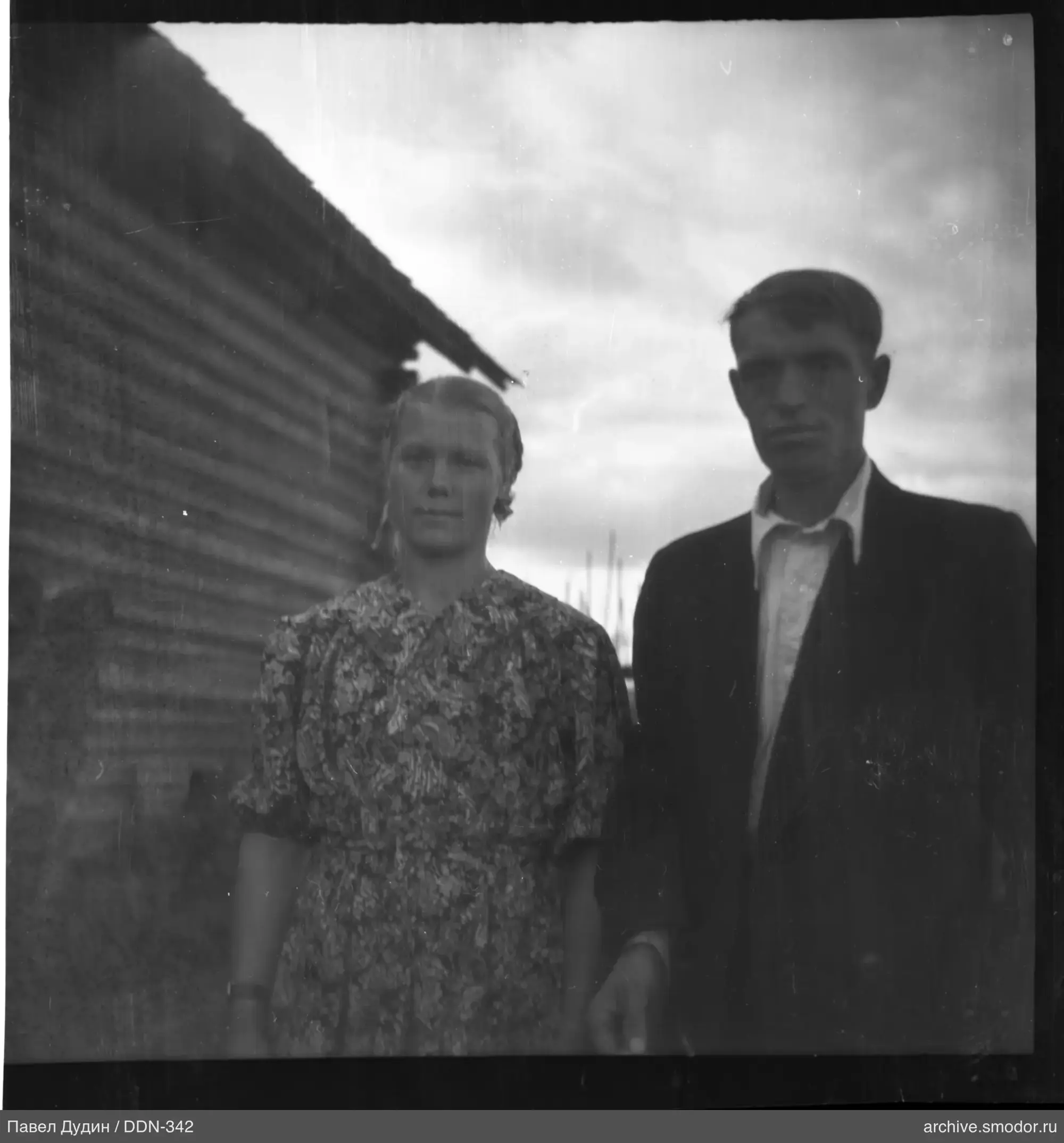 Portrait of a man and a woman against a wooden house