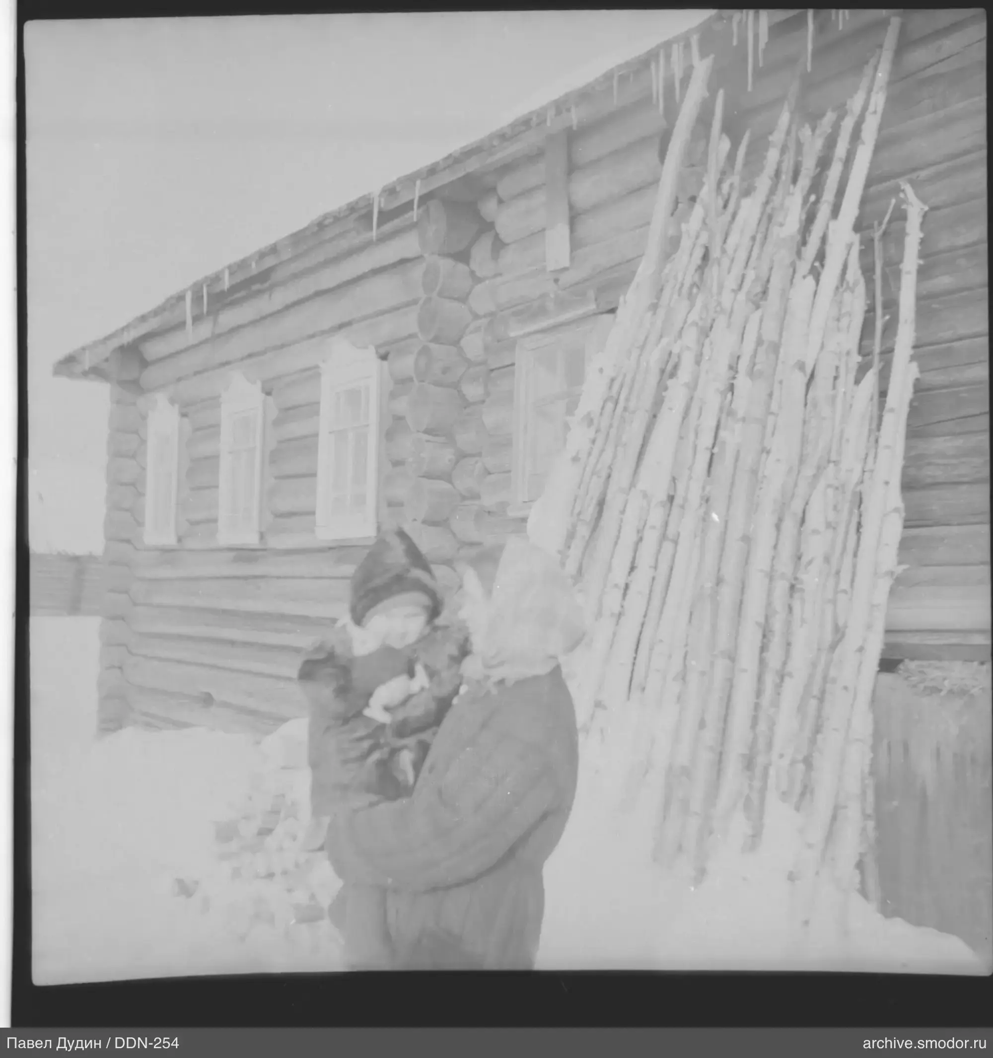 Frau mit Kind vor Holzhaus