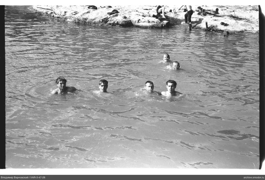 Men in water and on the shore by a rocky bank