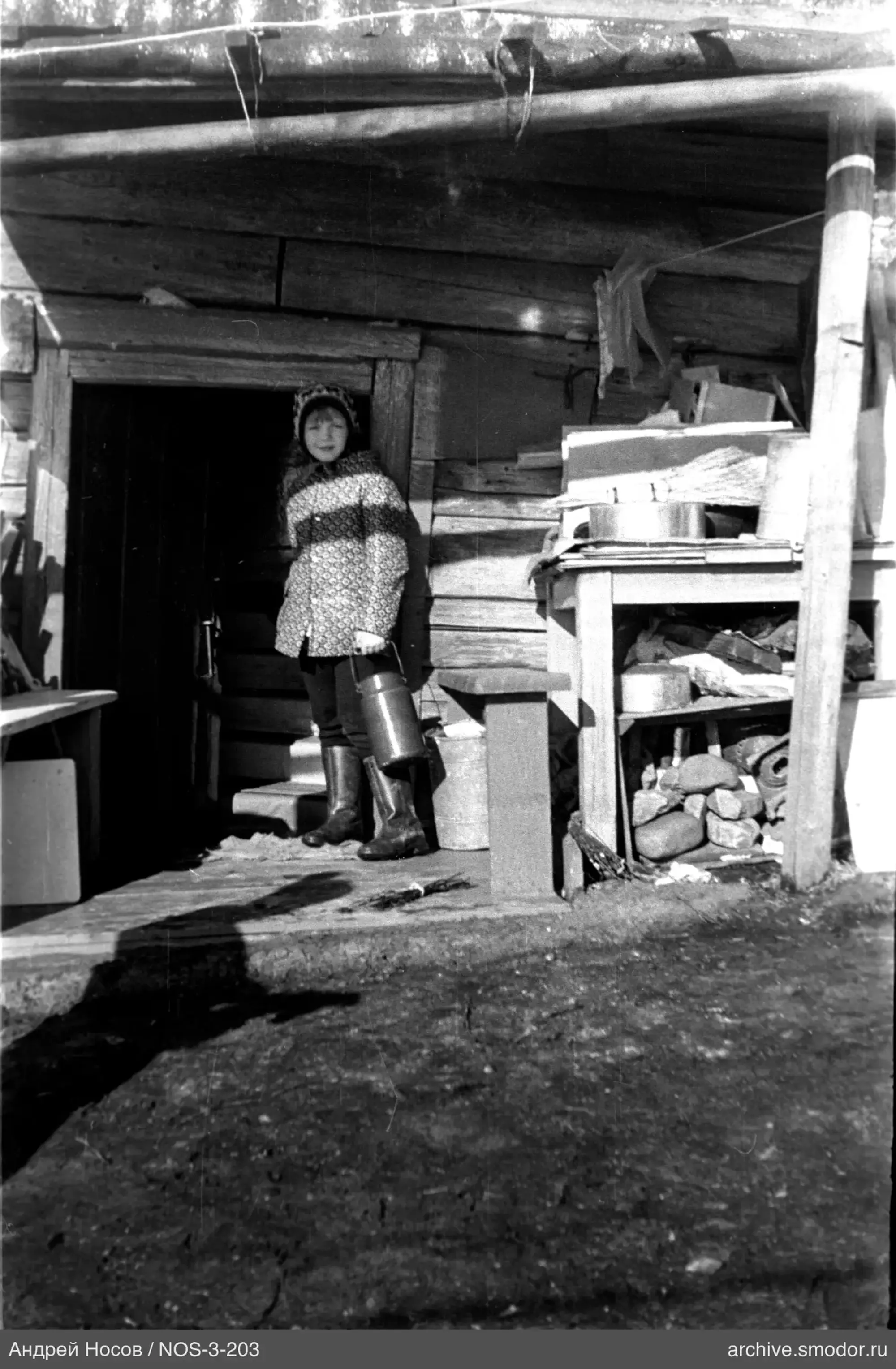 Frau mit Metallkanister am Holzhaus