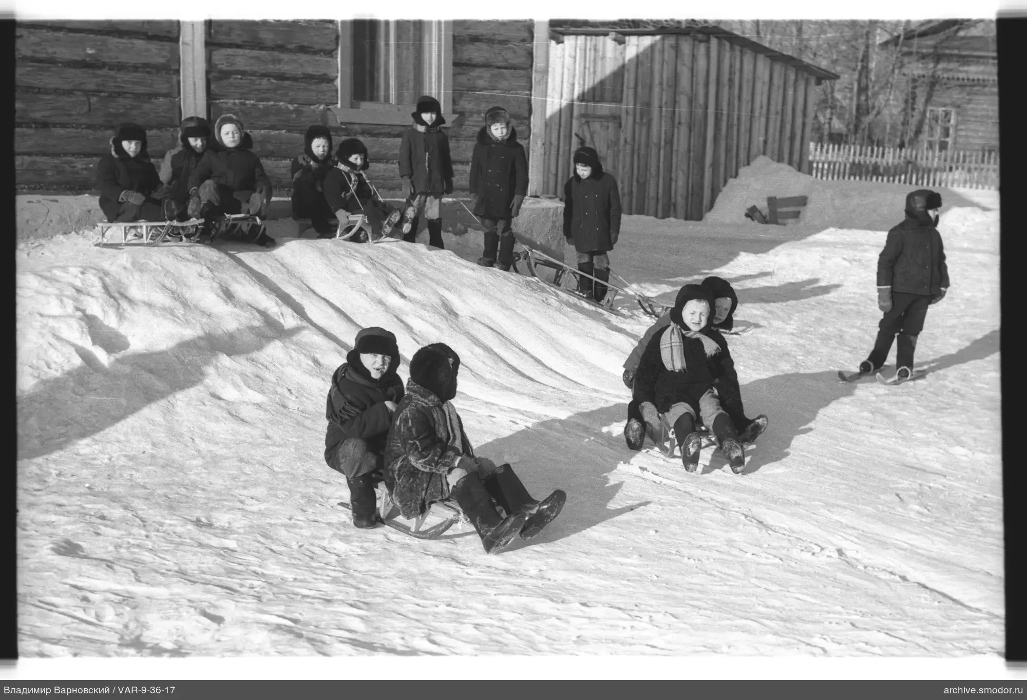 Kinder beim Rodeln und Skifahren bei einem Holzhaus