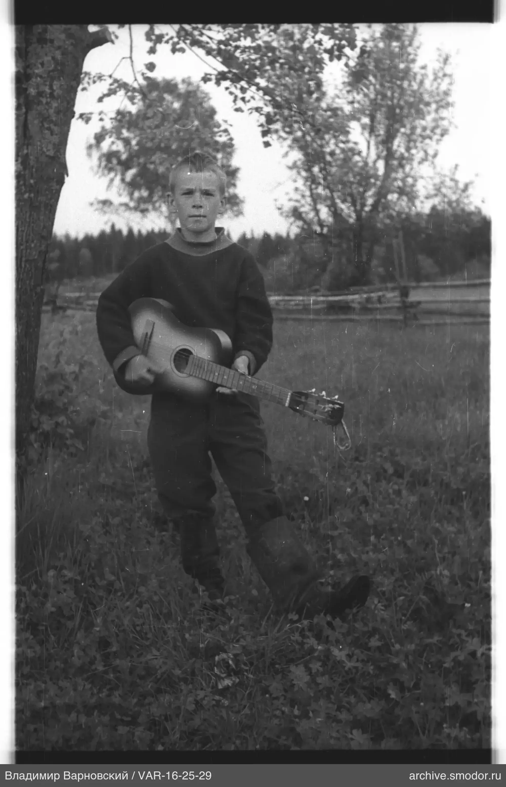Junge mit Gitarre neben einem Baum