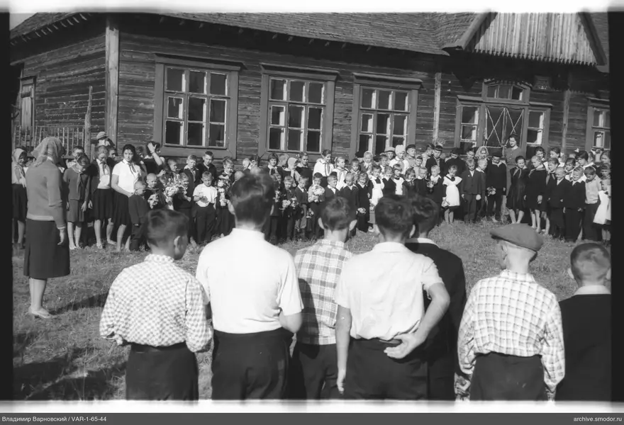 Gruppe von Kindern und Erwachsenen vor einem Holzgebäude