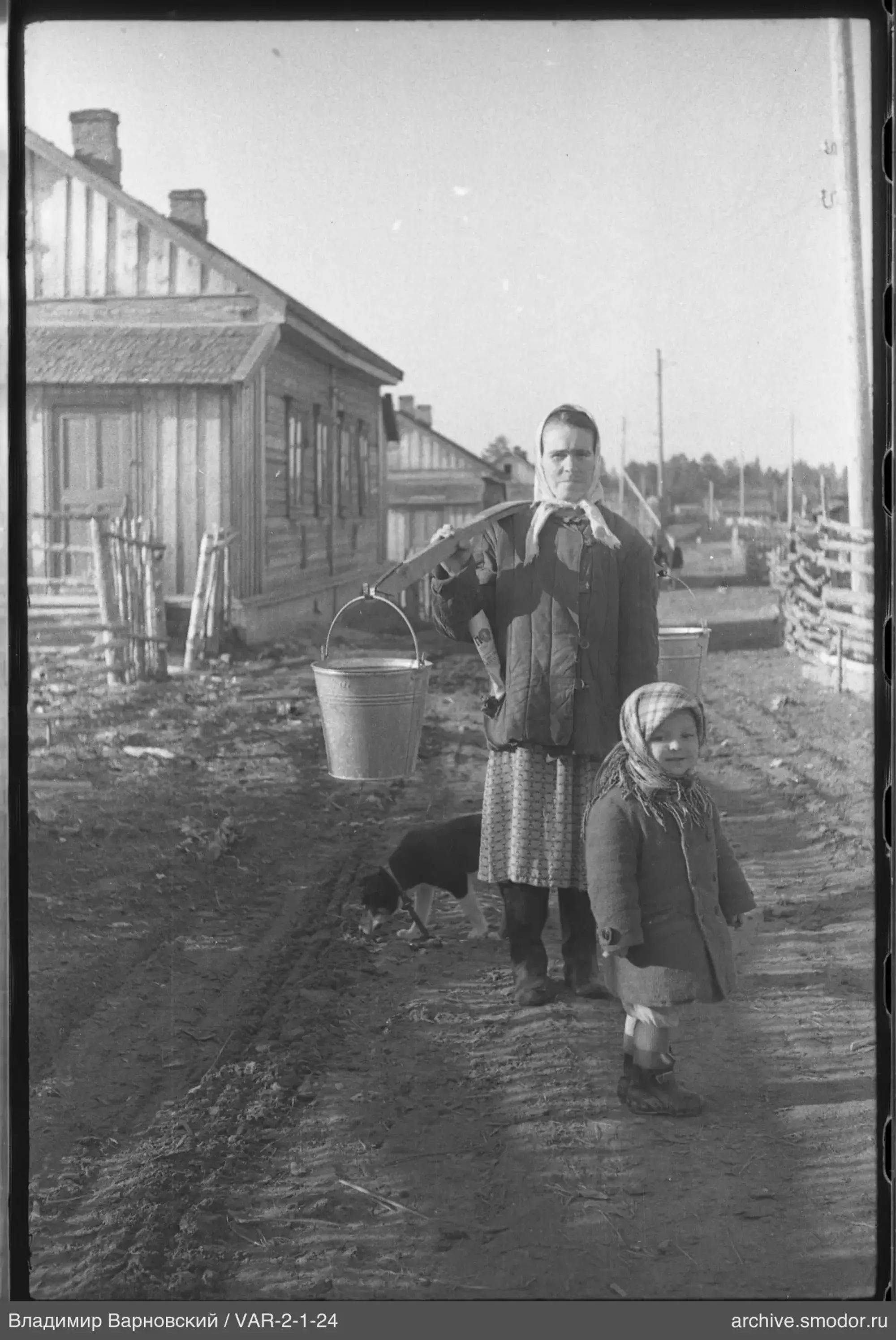 Женщина с коромыслом и ребёнок у деревянных домов