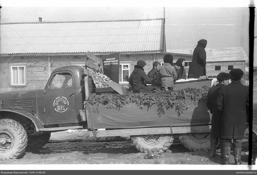 Грузовой автомобиль с людьми у деревянного дома