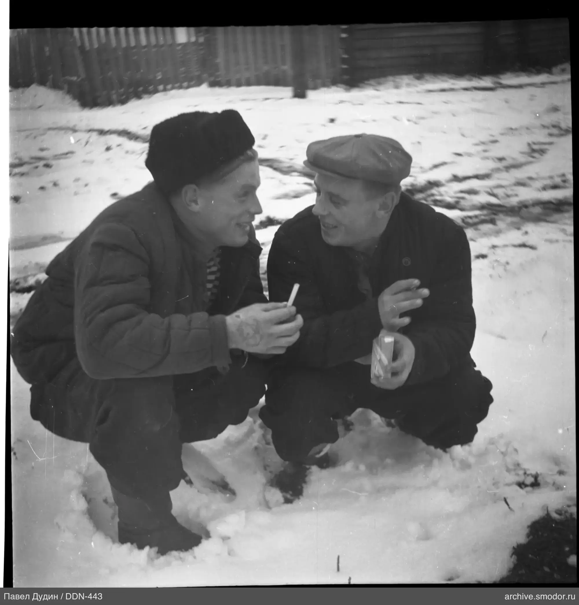 Two men sitting on snow with cigarettes