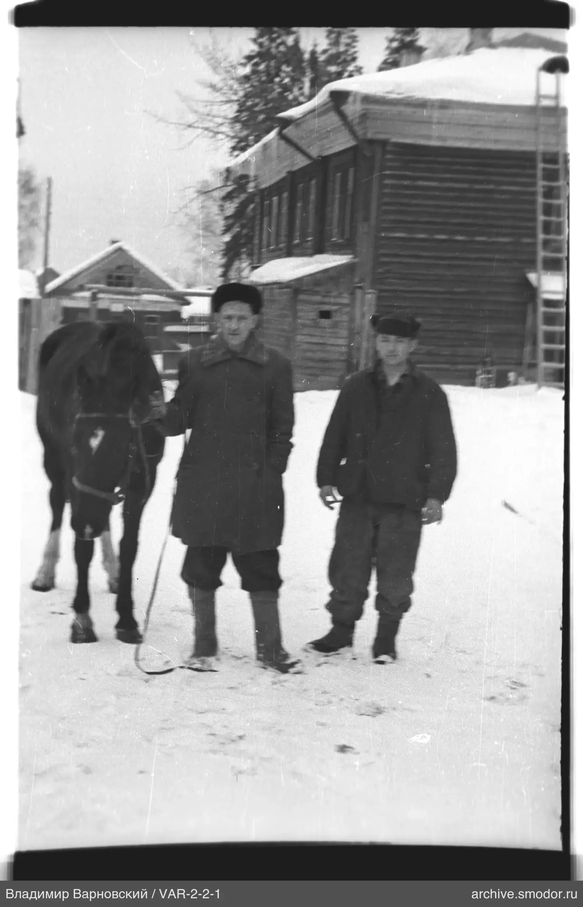 Zwei Männer mit einem Pferd vor einem Holzhaus