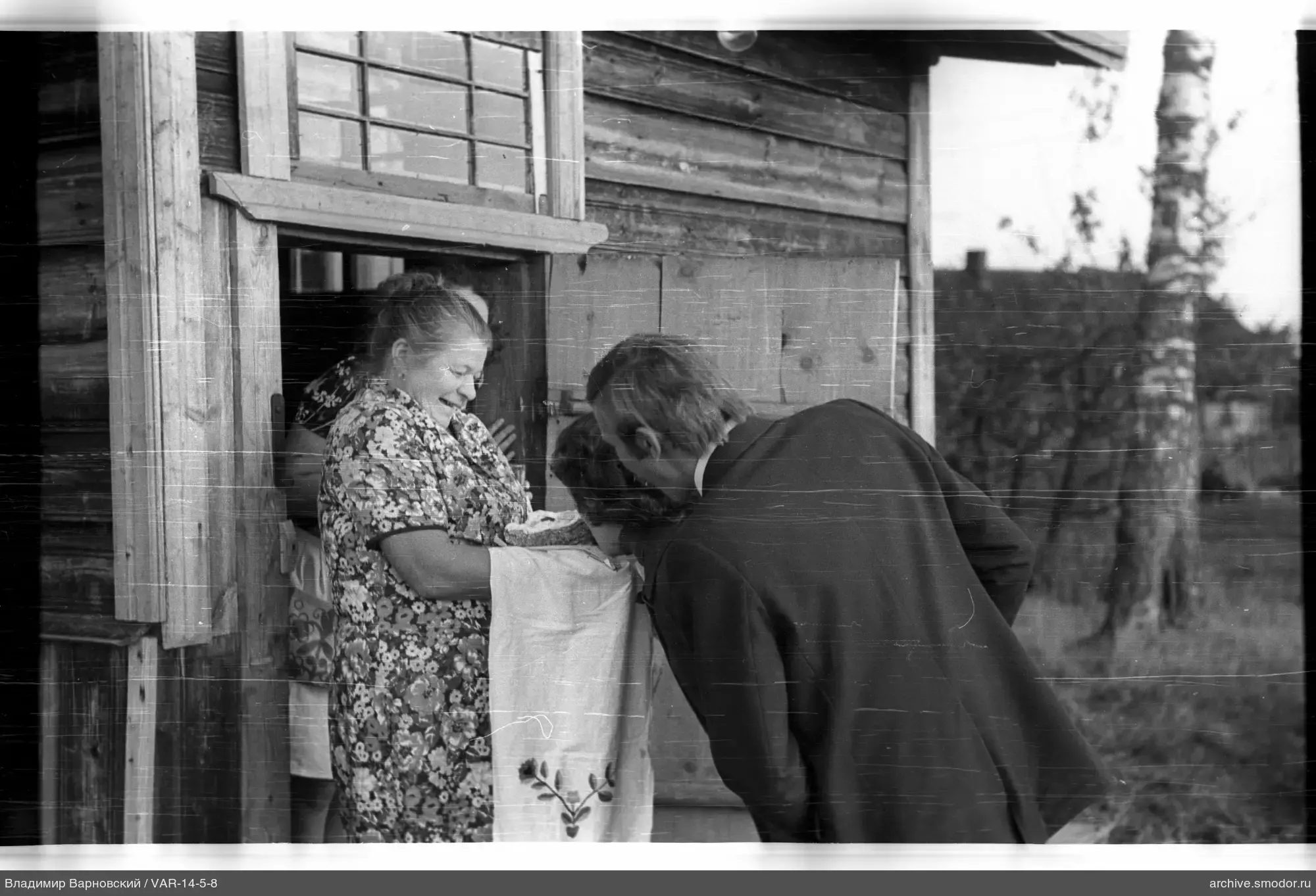 Mann und Frauen vor Holzhaus