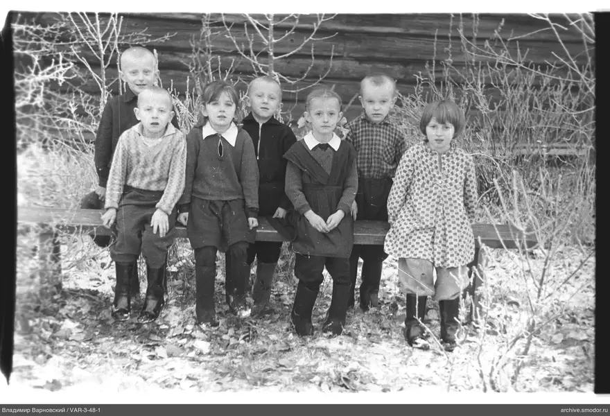 Gruppe von Kindern auf einer Bank vor einer Holzwand