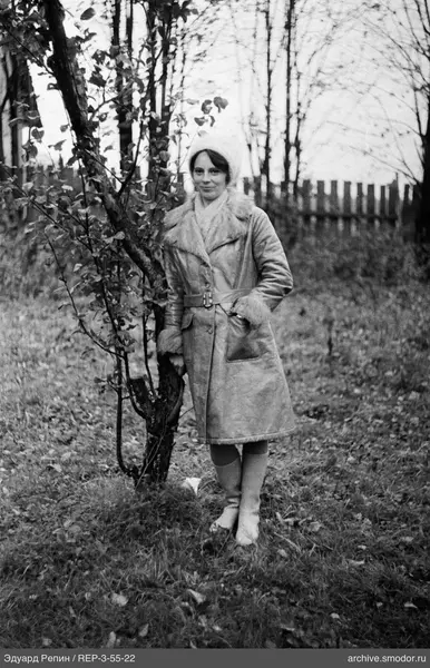 Frau an einem Baum in Mantel und Mütze