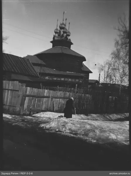 Женщина с тростью у деревянного здания с куполами