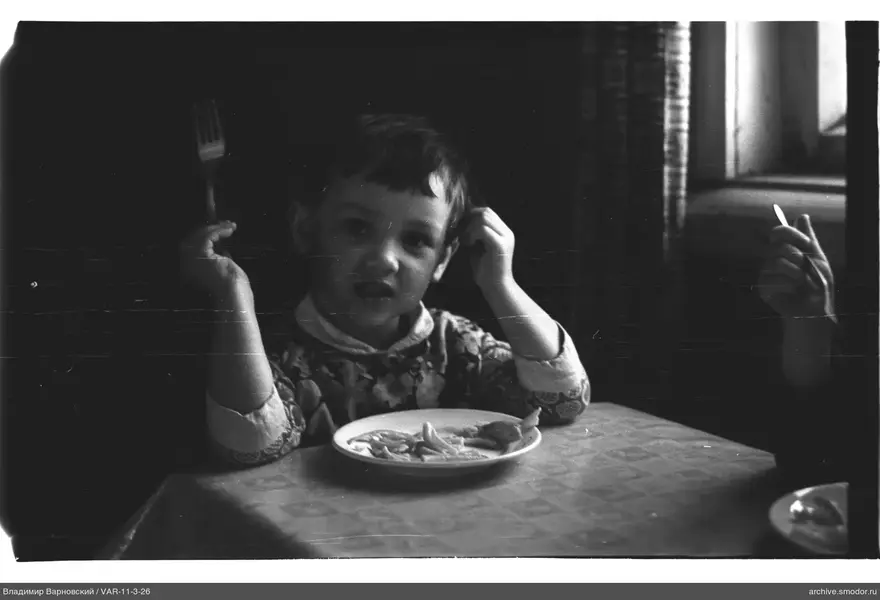 Child sitting at a table with food and hand to head