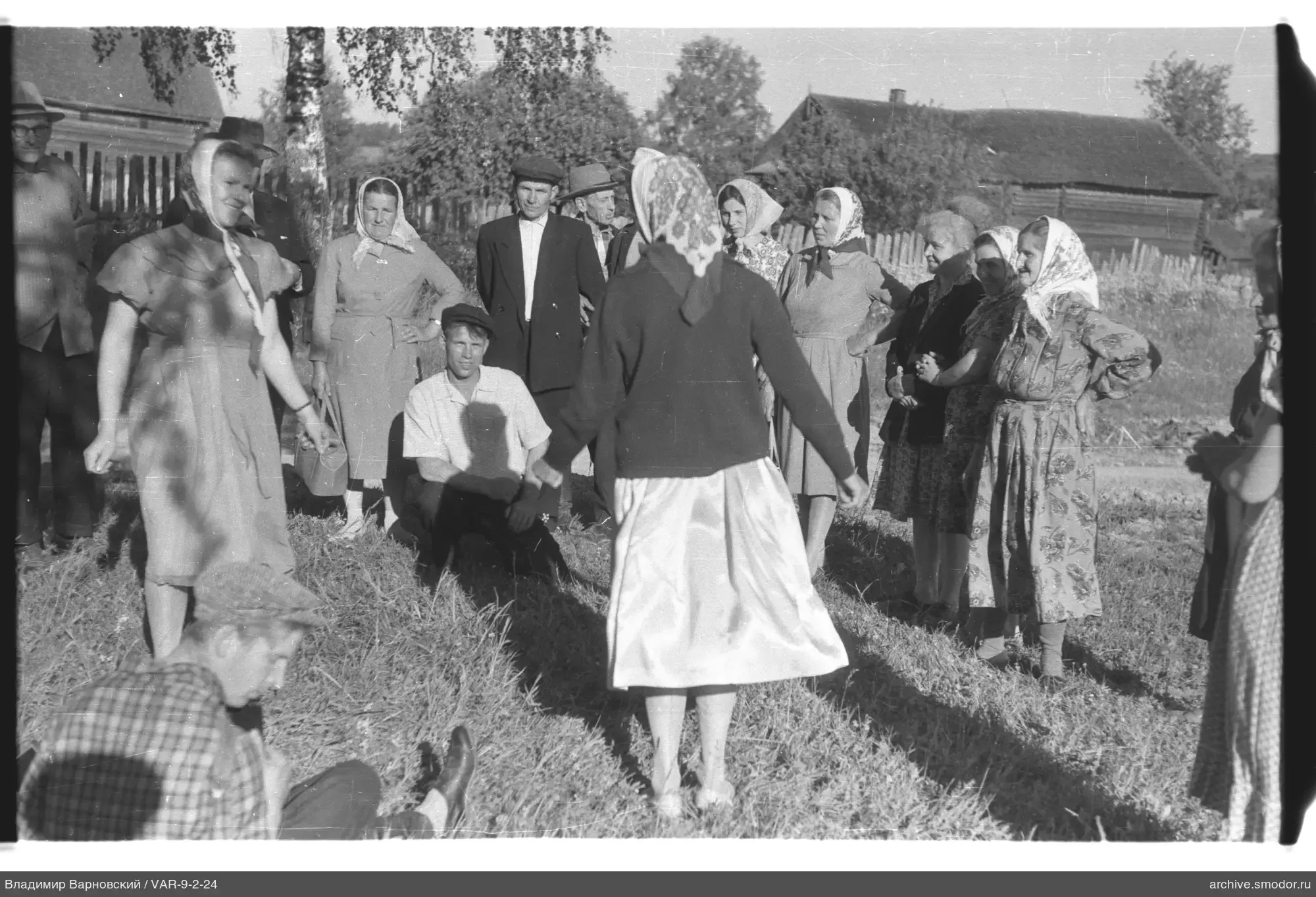Gruppe von Menschen auf Gras bei Holzbauten