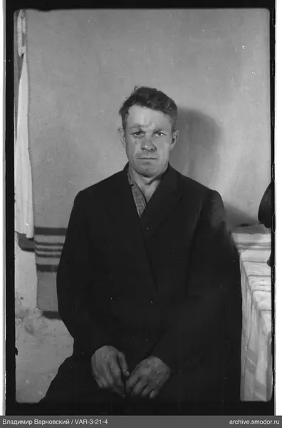Seated man in dark jacket and checkered shirt