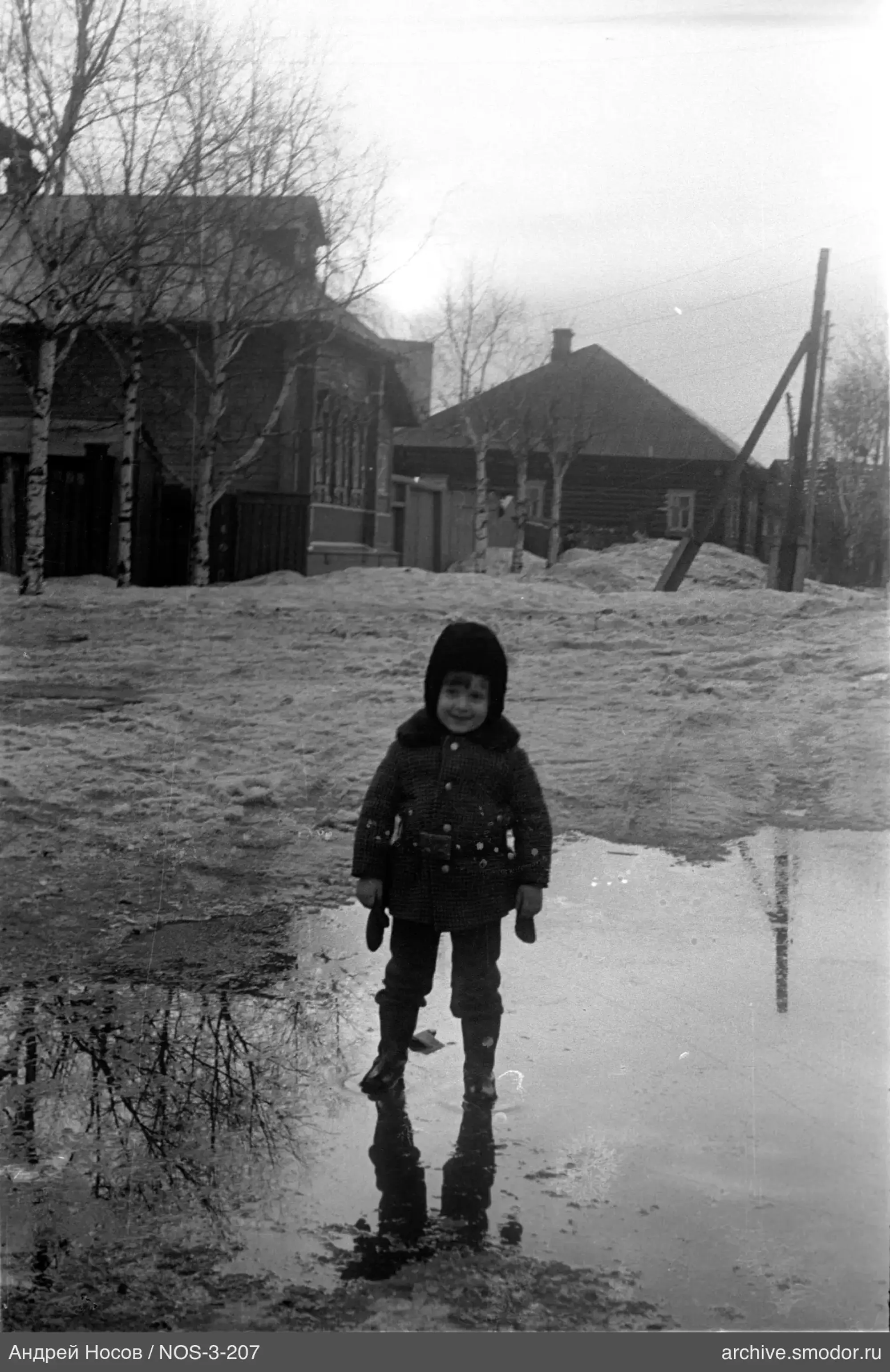 Kind in warmer Kleidung bei Holzhäusern