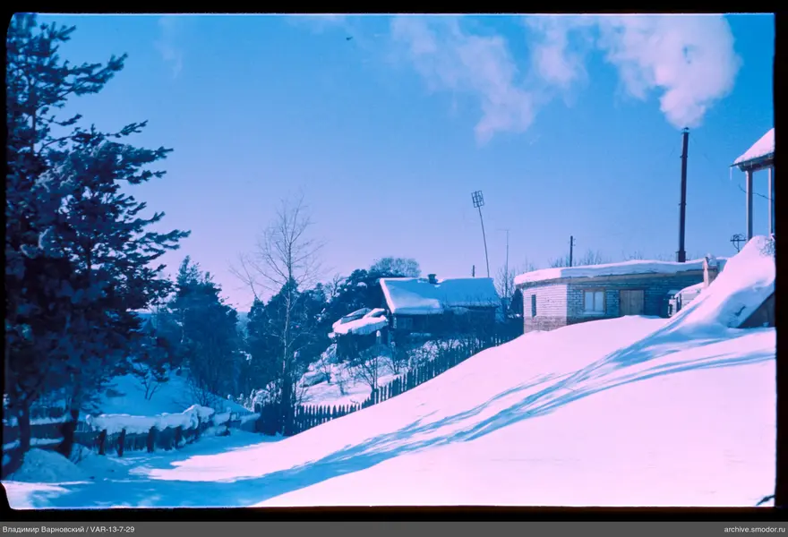 Snow-covered slope with buildings and fence