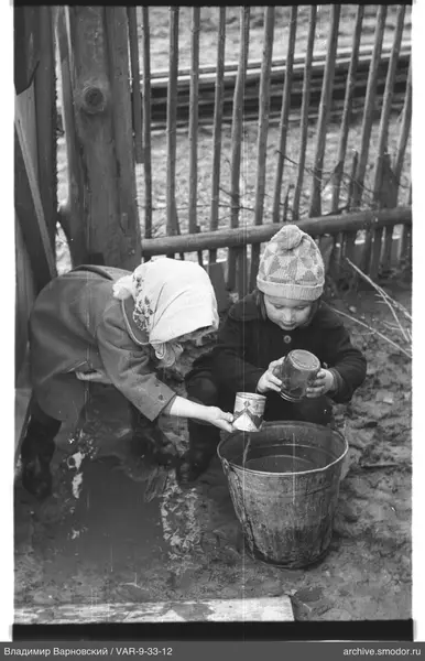 Zwei Kinder mit Gläsern neben einem Wasserbottich
