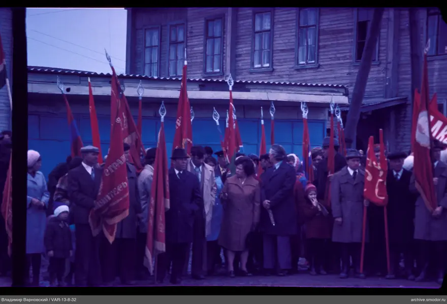 Gruppe von Menschen vor einem Holzgebäude mit Fahnen