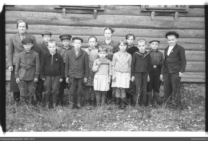 Gruppenporträt von Kindern und Frau vor Holzhaus