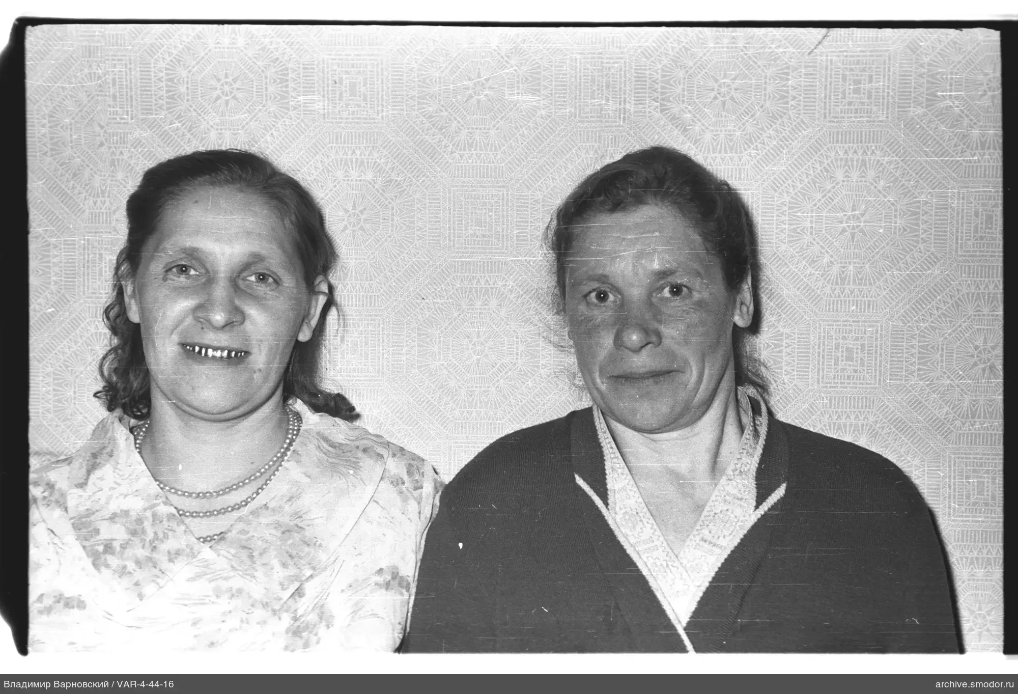 Two women in a portrait against patterned wallpaper