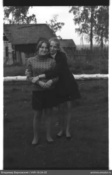 Zwei Frauen auf Gras vor einem Holzhaus