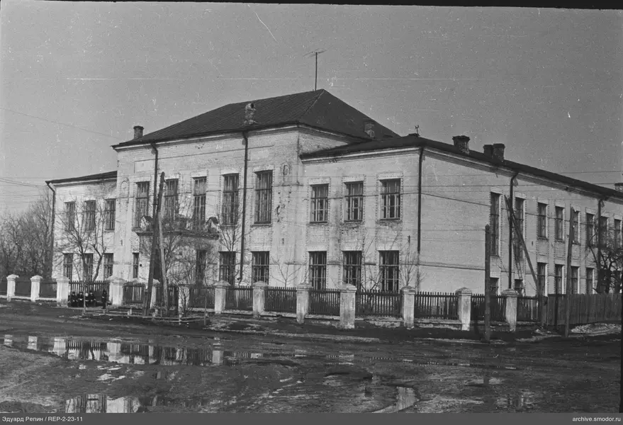 Zweistöckiges Backsteingebäude mit Zaun und Bäumen