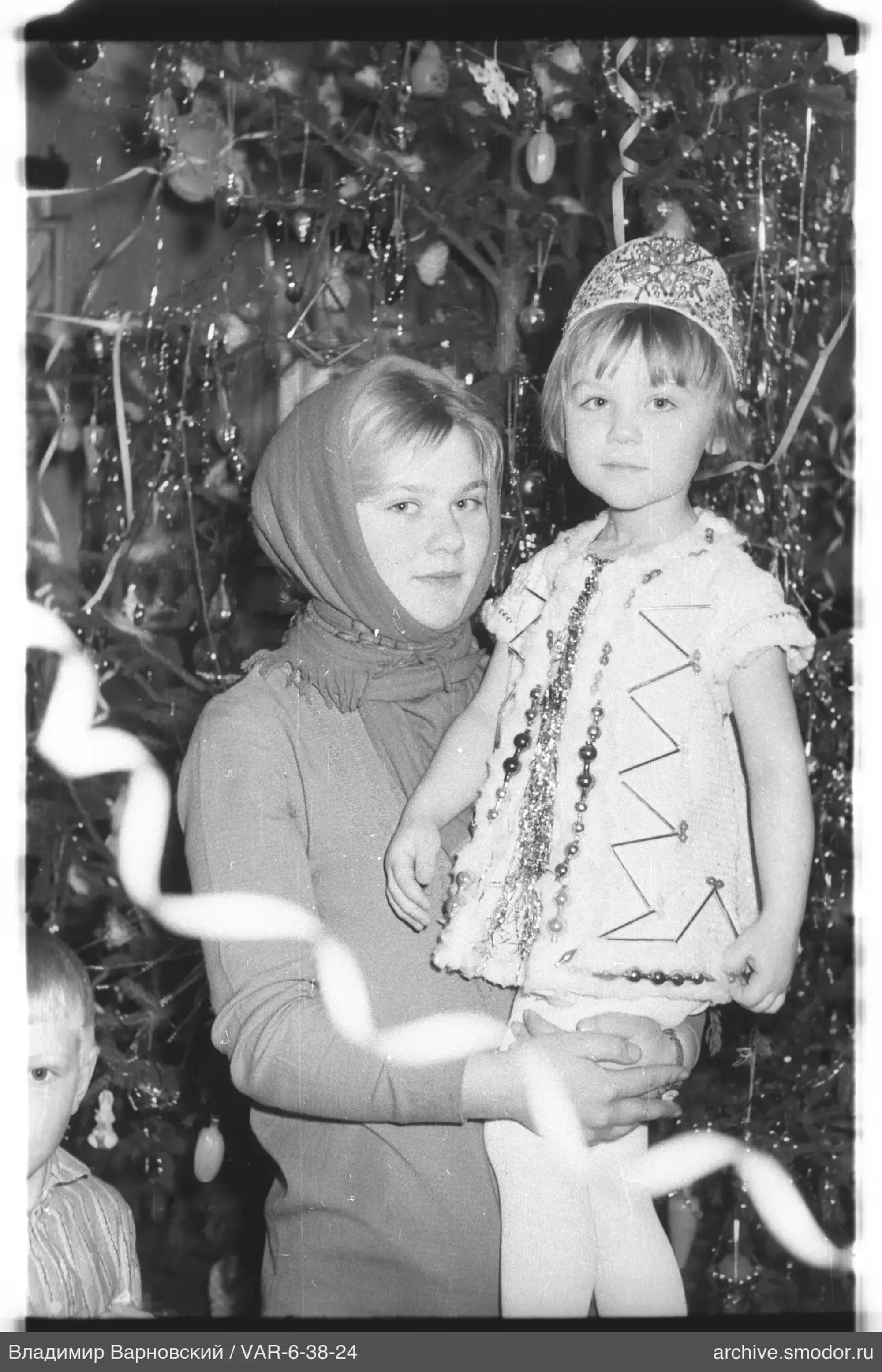 Frau mit Mädchen vor geschmücktem Weihnachtsbaum