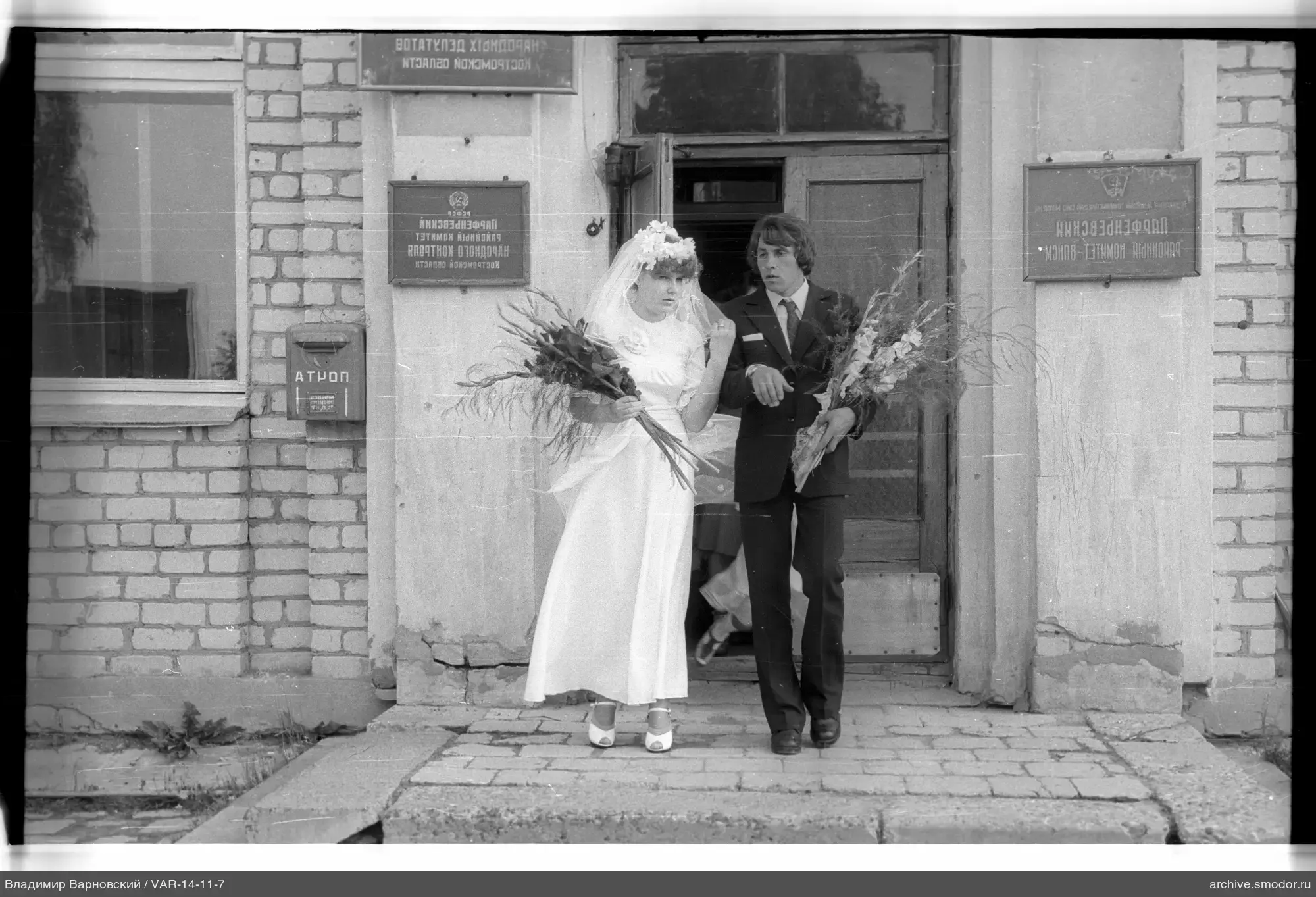 Frau mit Blumenstrauß und Mann beim Verlassen des Gebäudes