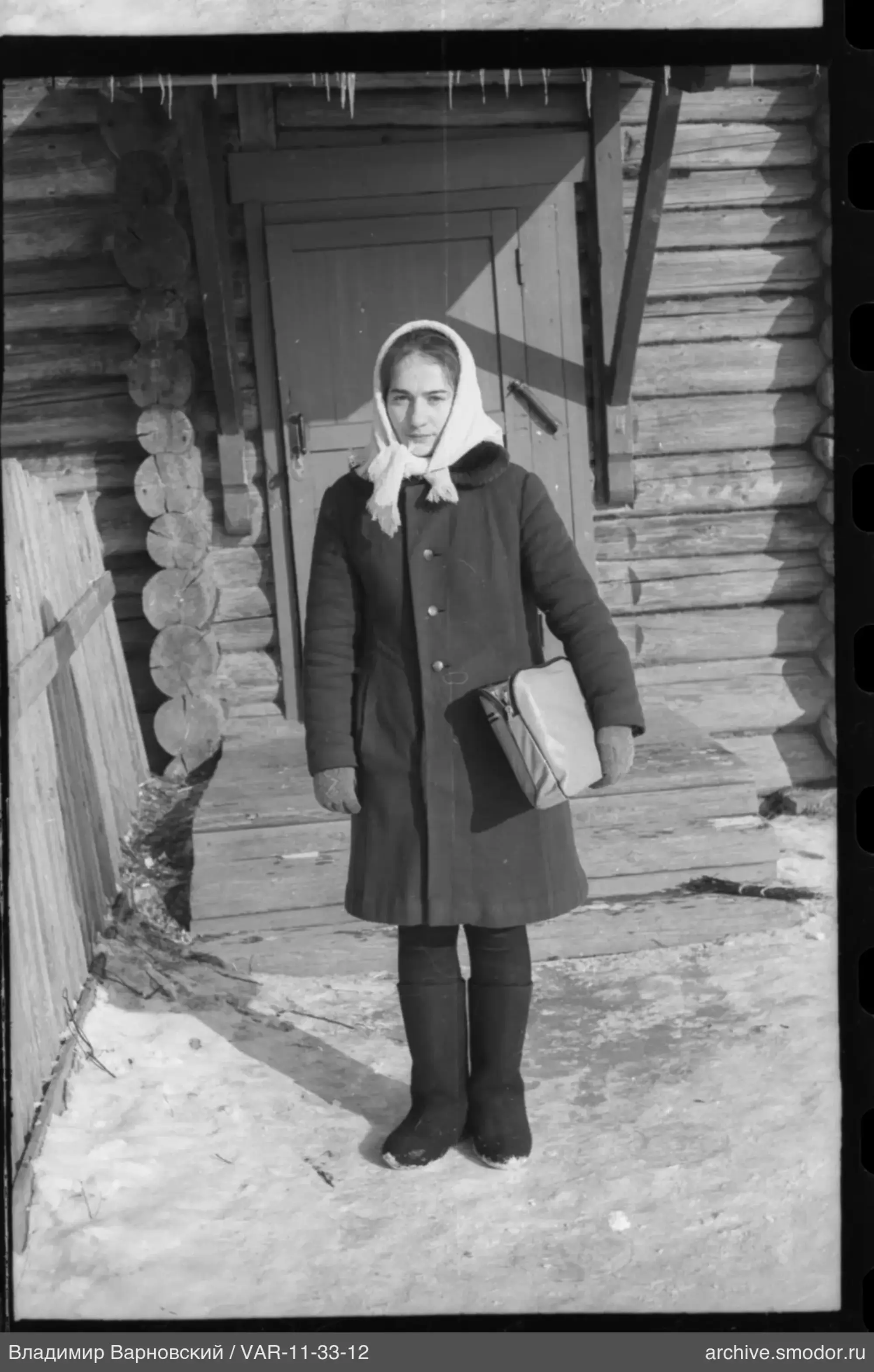 Woman standing on snow in front of a wooden house
